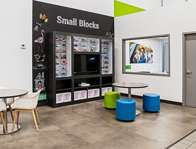 The kids' area of an EchoPark store has colorful blue and green seating and tables, with toy cars on display and children's books to keep the little ones occupied.