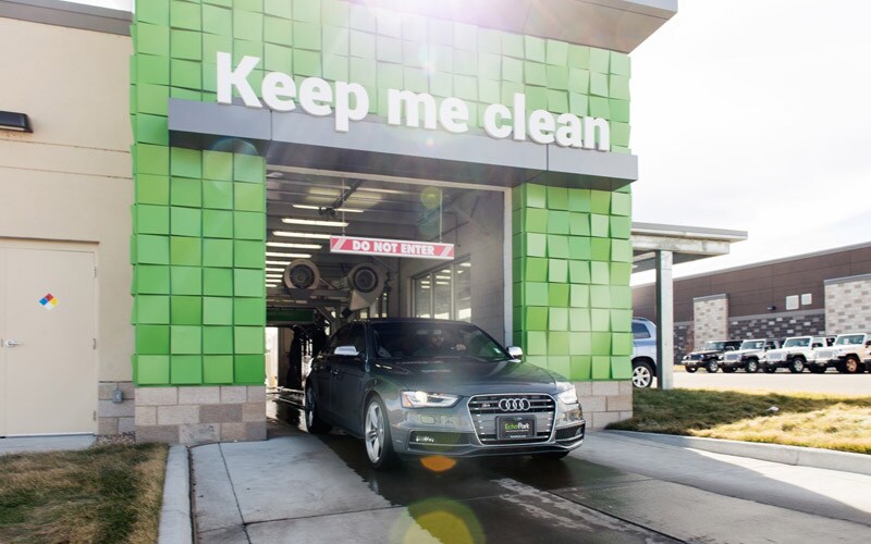 Image shows the front of a car wash at a Denver-area EchoPark. A car is exiting the car wash. A sign about the exit of the car wash says “Keep Me Clean.”
