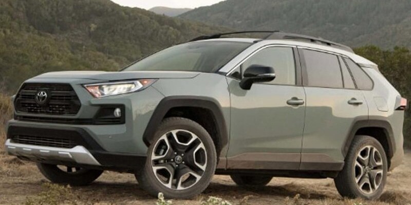 Image shows a light green Toyota RAV4 with a background of tree-covered mountains.