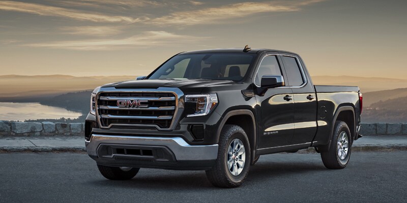 Image shows a blue GMC Sierra driving a highway in the mountains and alongside a lake.