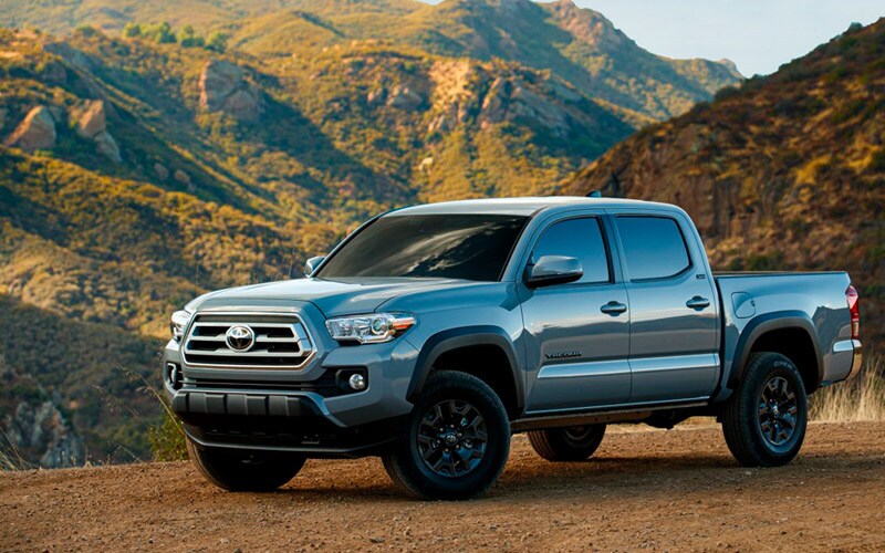 Image shows a silver Toyota Tacoma with mountains in the background.