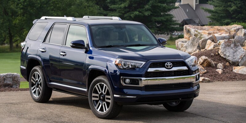 Image shows a blue Toyota 4Runner on parked on pavement with trees in the background.