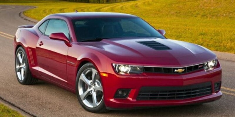 Image shows a red Chevrolet Camaro parked with a curved road and grass in the background.