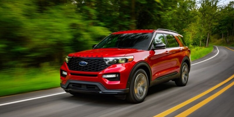 Image shows a red Ford Explorer driving down a tree-lined highway.
