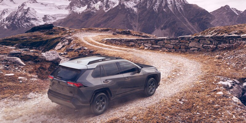 Image shows a Toyota RAV4 driving up a dirt road toward snow-covered mountains.