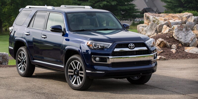 Image shows a blue Toyota 4Runner on parked on pavement with trees in the background.
