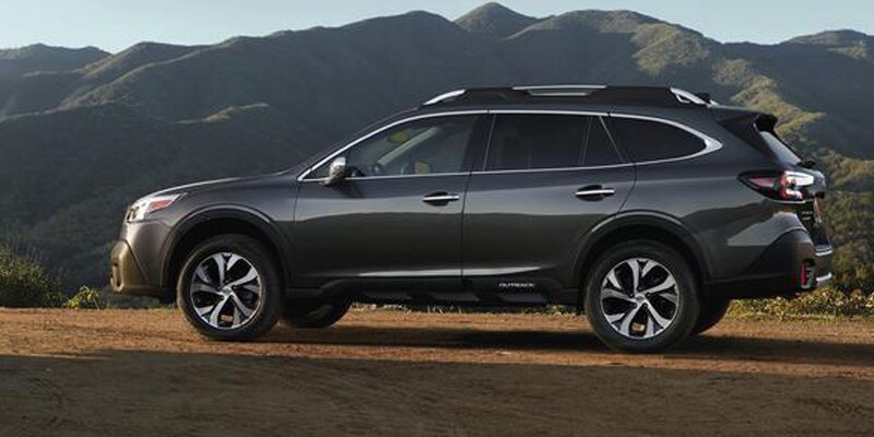 Image is of a silver Subaru Outback with mountain range in the background.