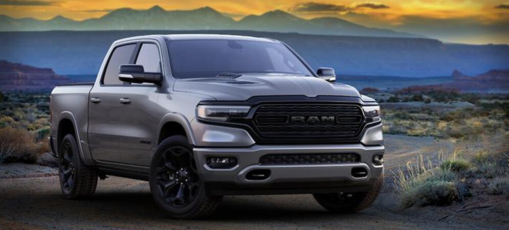 Image shows a silver Ram 1500 pickup truck in a desert landscape at sunset. There are mountains in the background.
