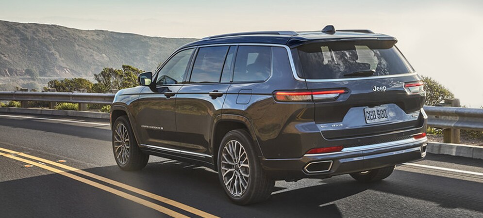 Image shows a dark gray Jeep Grand Cherokee driving on a highway, overlooking a valley with fog in the background.