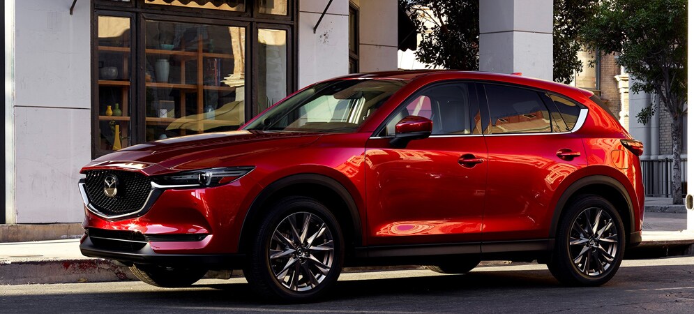 Image shows a red Mazda CX-5 parked outside a storefront in a city.