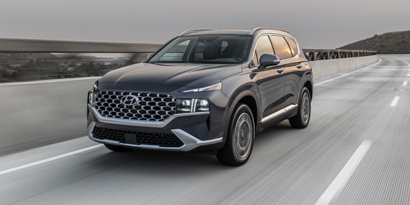 Image shows a Hyundai Santa Fe driving on a highway bridge with a valley in the background.