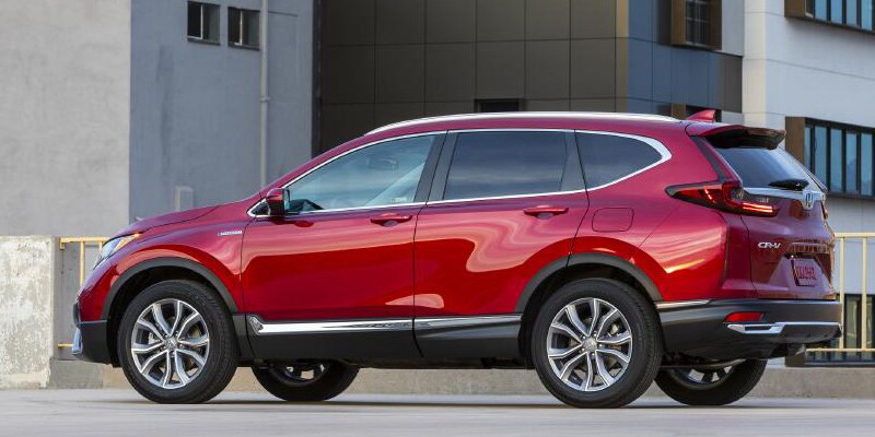 Image shows a red Honda CR-V parked in front of a modern city building.
