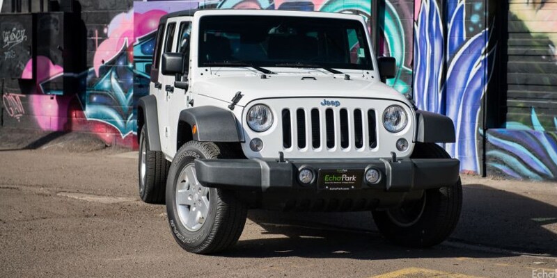 Image shows a white Jeep Wrangler parked in front of a wall adorned with a bright pink, purple and turquoise abstract mural.