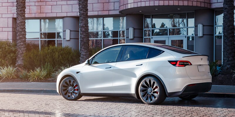 A white Tesla Y parked in front of a modern office building.