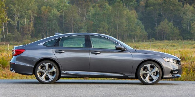 Image shows gray Honda Accord parked on pavement, with trees and mountains in the background.