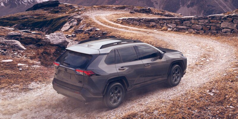 Image shows a Toyota RAV4 driving up a dirt road toward snow-covered mountains.