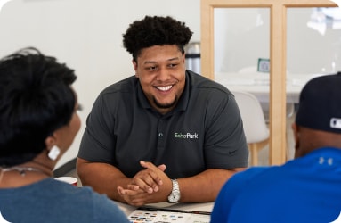 Male Experience Guide smiling across the table from two used car shoppers inside an EchoPark Automotive store