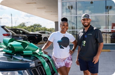 Male Experience Guide and female happy owner standing outside next to quality used car with a giant green bow on it in front of EchoPark Automotive store location