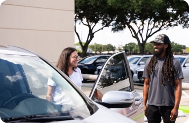 Woman smiling next to open driver’s door of quality used car with a male EchoPark Experience Guide happily standing nearby