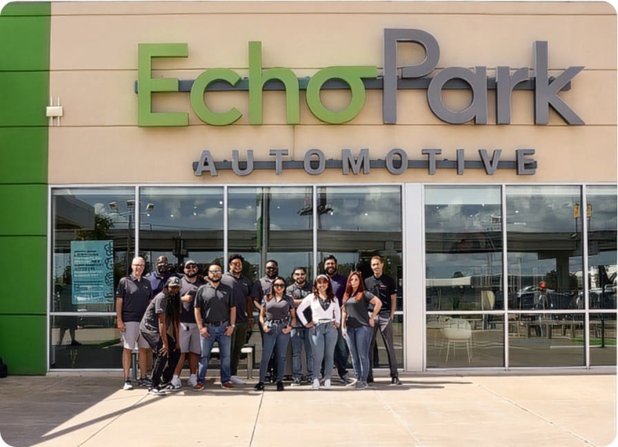 Exterior EchoPark Automotive storefront featuring 13 Experience Guides standing together as a group, smiling, and posing for photograph