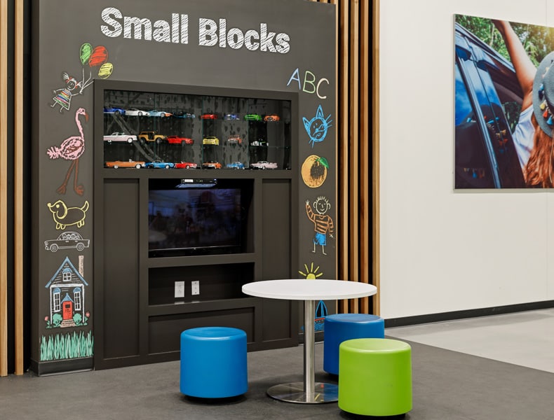 The kids' area of an EchoPark store has colorful blue and green seating and tables, with toy cars on display and children's books to keep the little ones occupied.