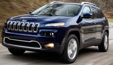 Image shows a dark blue Jeep Cherokee driving along a mountain highway.