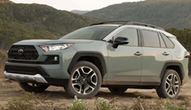 Image shows a light green Toyota RAV4 with a background of tree-covered mountains.