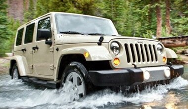 Image shows a tan Jeep Wrangler crossing a shallow stream with rocks.