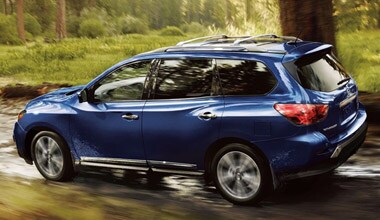 Image shows a blue Nissan Pathfinder driving trough the woods.