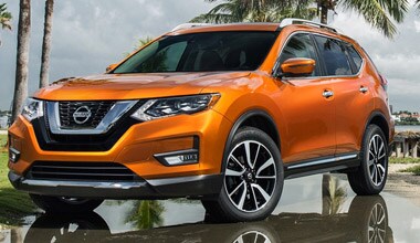 Image shows an orange Nissan Rogue parked wet pavement, with palm trees and a gray sky in the background.