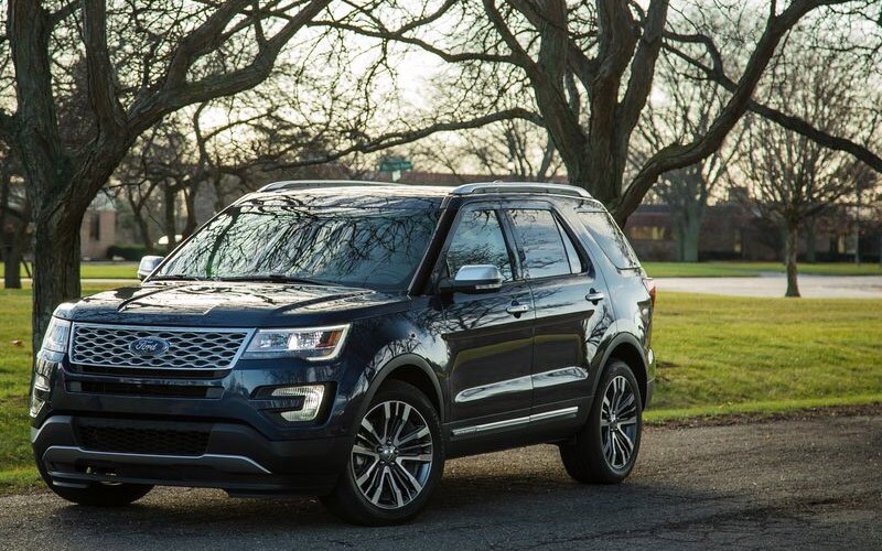 Image shows a blue Ford Explorer parked on a street with trees in the background.