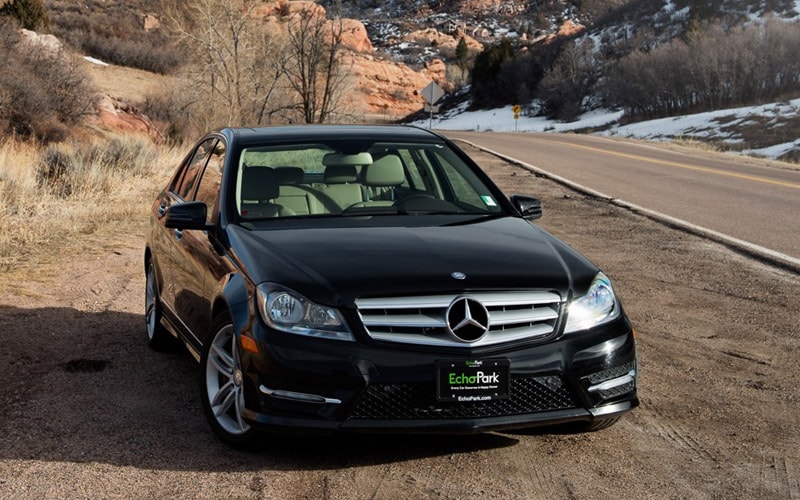 Image shows a black Mercedes-Benz parked beside a mountain highway. The car has an EchoPark tag on the front.