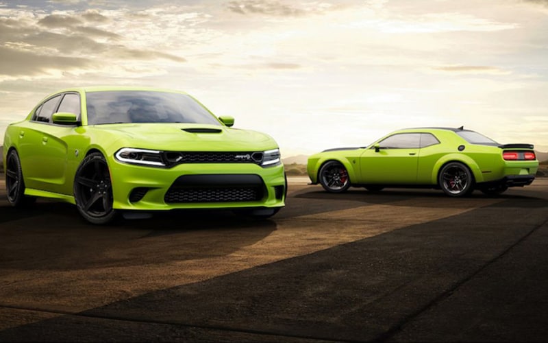 Image shows a sublime green-colored Dodge Charger and Challenger at a low-angled aggressive stance on asphalt with dramatic lighting and skies in the background. 