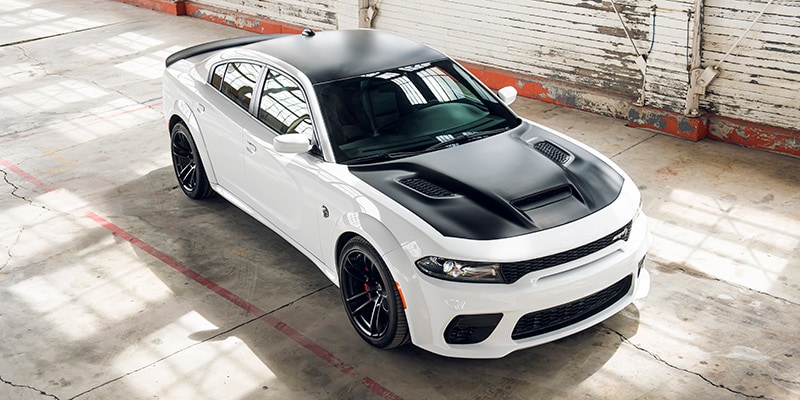 Image shows a menacingly white and black Dodge Hellcat in an aggressive stance bathed sunlight beaming in from grungy warehouse windows.