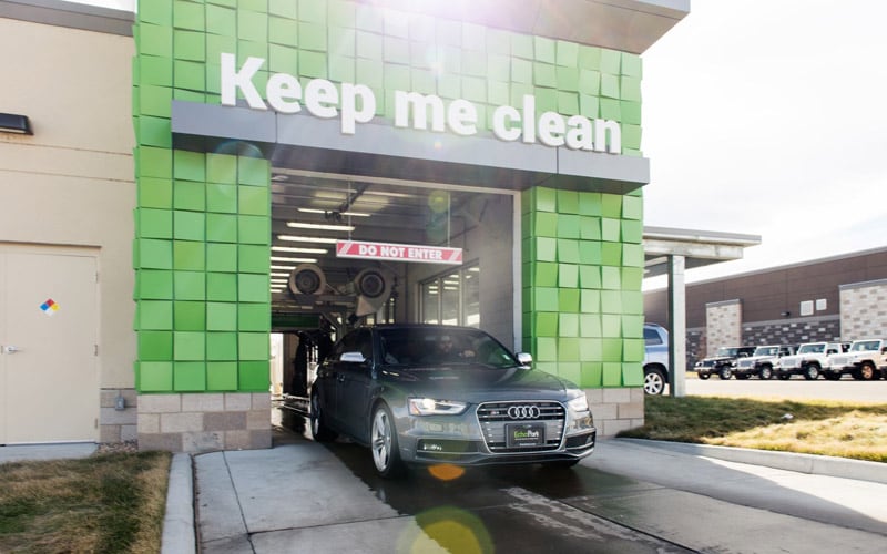 Image shows the front of a car wash at a Denver-area EchoPark. A car is exiting the car wash. A sign about the exit of the car wash says “Keep Me Clean.”