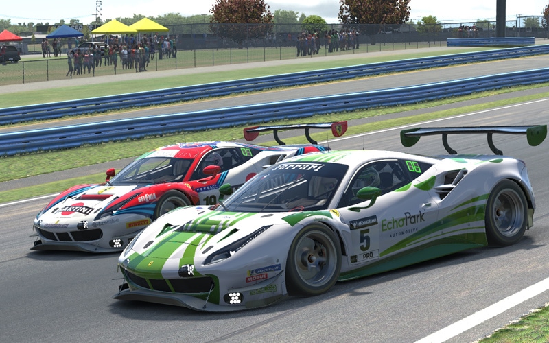 Image shows a white Ferrari 488 EVO with green stripes and the EchoPark Automotive logo on the side in the foreground. It’s running beside a white race car with blue and red stripes on a paved track with guardrails in the background.