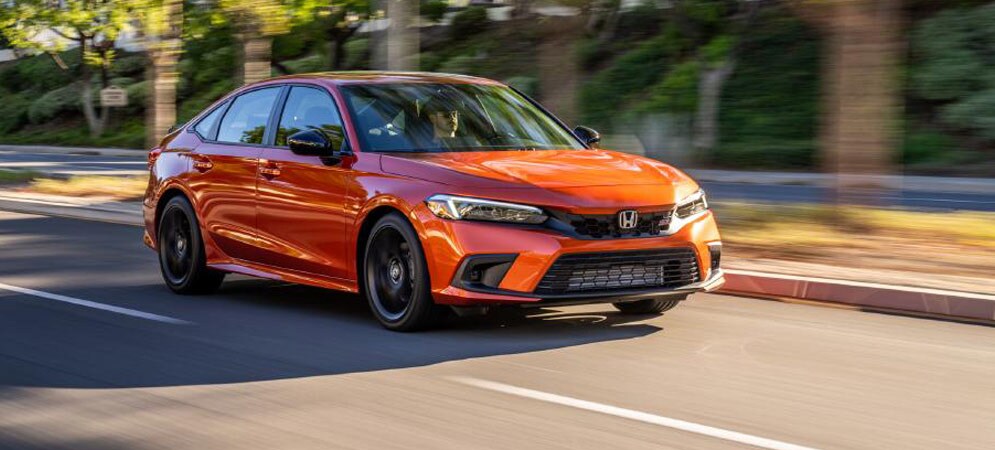 Image shows a bright orange Honda Civic driving on a road with trees in the background.