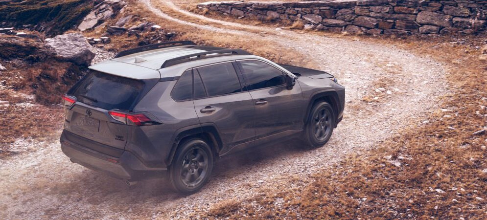 Image shows a Toyota RAV4 driving up a dirt road toward snow-covered mountains.