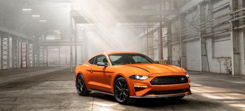 Image shows an orange Ford Mustang parked in an empty warehouse.