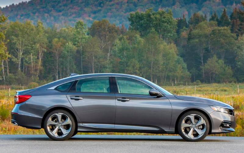 Image shows gray Honda Accord parked on pavement, with trees and mountains in the background.