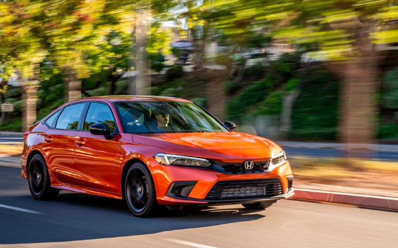 Image shows orange Honda Civic driving down a tree-lined street.