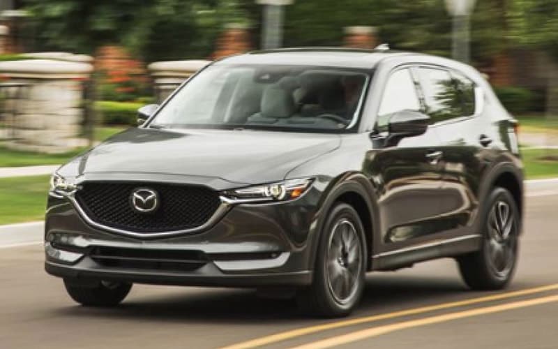 Image shows a black Mazda CX-5 driving down a highway past a house.