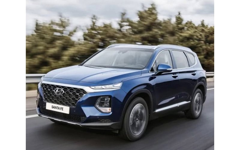 Image shows a blue Hyundai Santa Fe driving along a tree-lined highway.