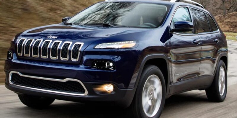 Image shows a dark blue Jeep Cherokee driving along a mountain highway.