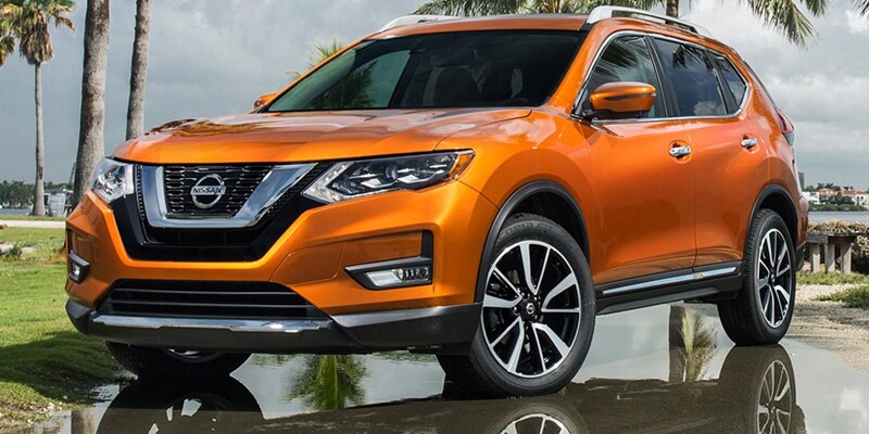 Image shows an orange Nissan Rogue parked wet pavement, with palm trees and a gray sky in the background.
