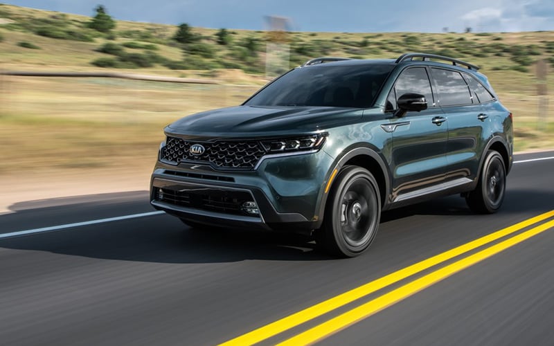 Image shows a dark green Kia Sorento driving down a highway in a desert.
