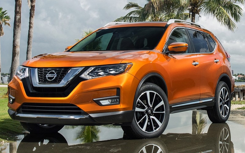 Image shows an orange Nissan Rogue parked wet pavement, with palm trees and a gray sky in the background.