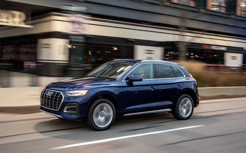 Image shows a dark blue Audi Q5 driving down a city street.