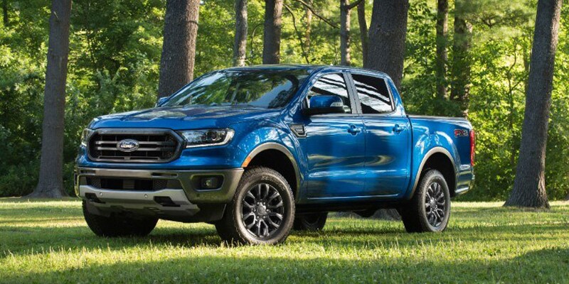 Image shows a blue Ford Ranger parked on grass in a wooded area.