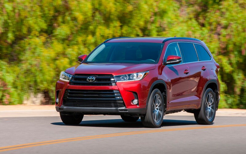 Image shoes a red Toyota Highlander parked on pavement with trees in the background.